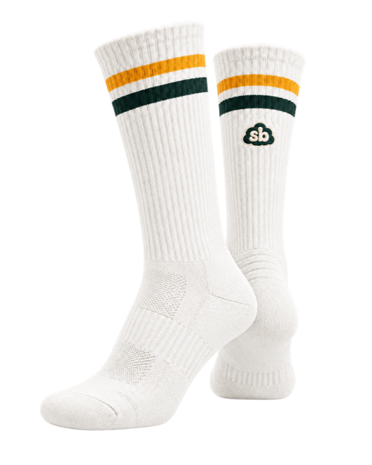 A pair of Sunday Best socks in Cream. A ribbed cream crew sock with two gold stripes and one dark green stripe at the welt, and the cloud sb mark on the outer calf.