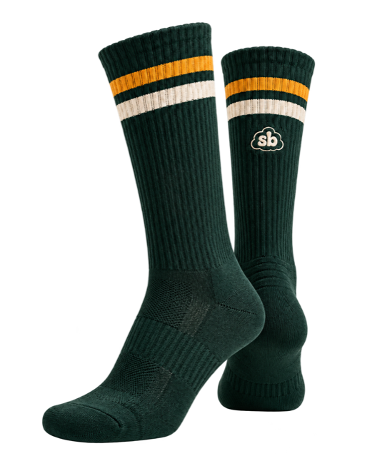 A pair of Sunday Best socks in Forest. A ribbed dark green crew sock with two gold stripes and one cream stripe at the welt, and the cloud sb mark on the outer calf.